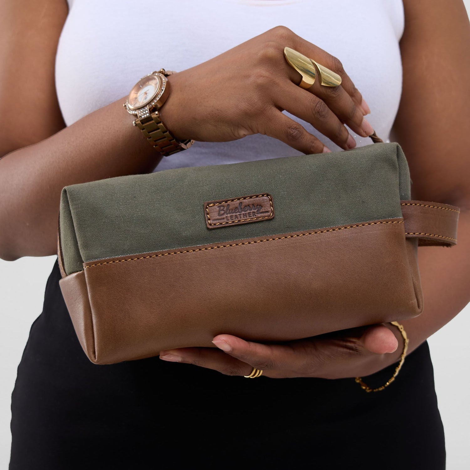 Person holding a green and brown clutch bag with a plain background