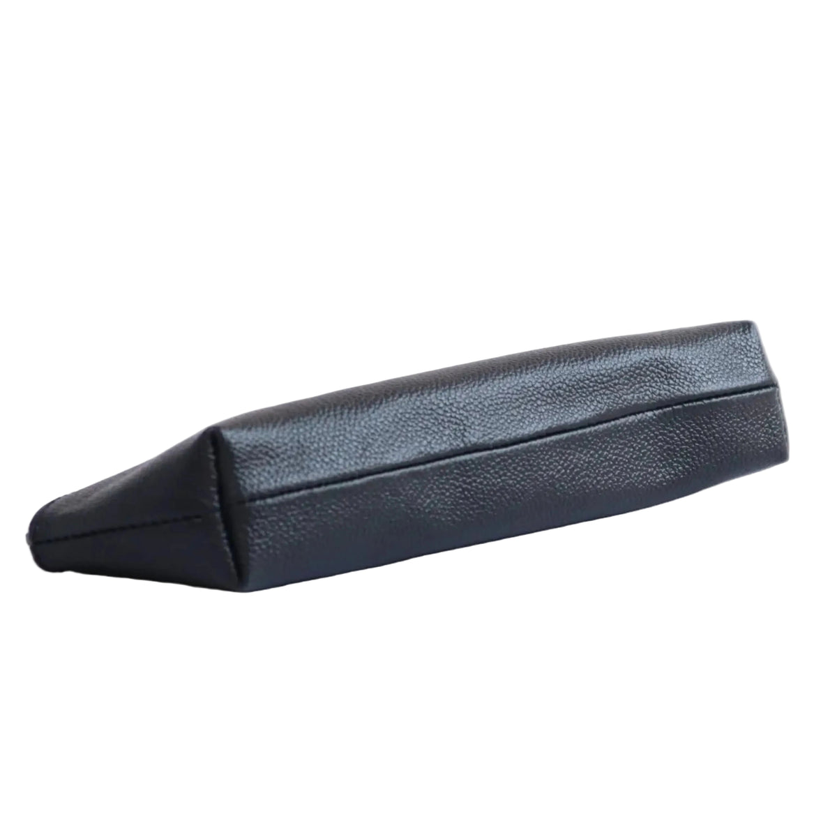 A black pebbled leather triangular wedge support cushion, shown from a side angle against a solid pale pink background.