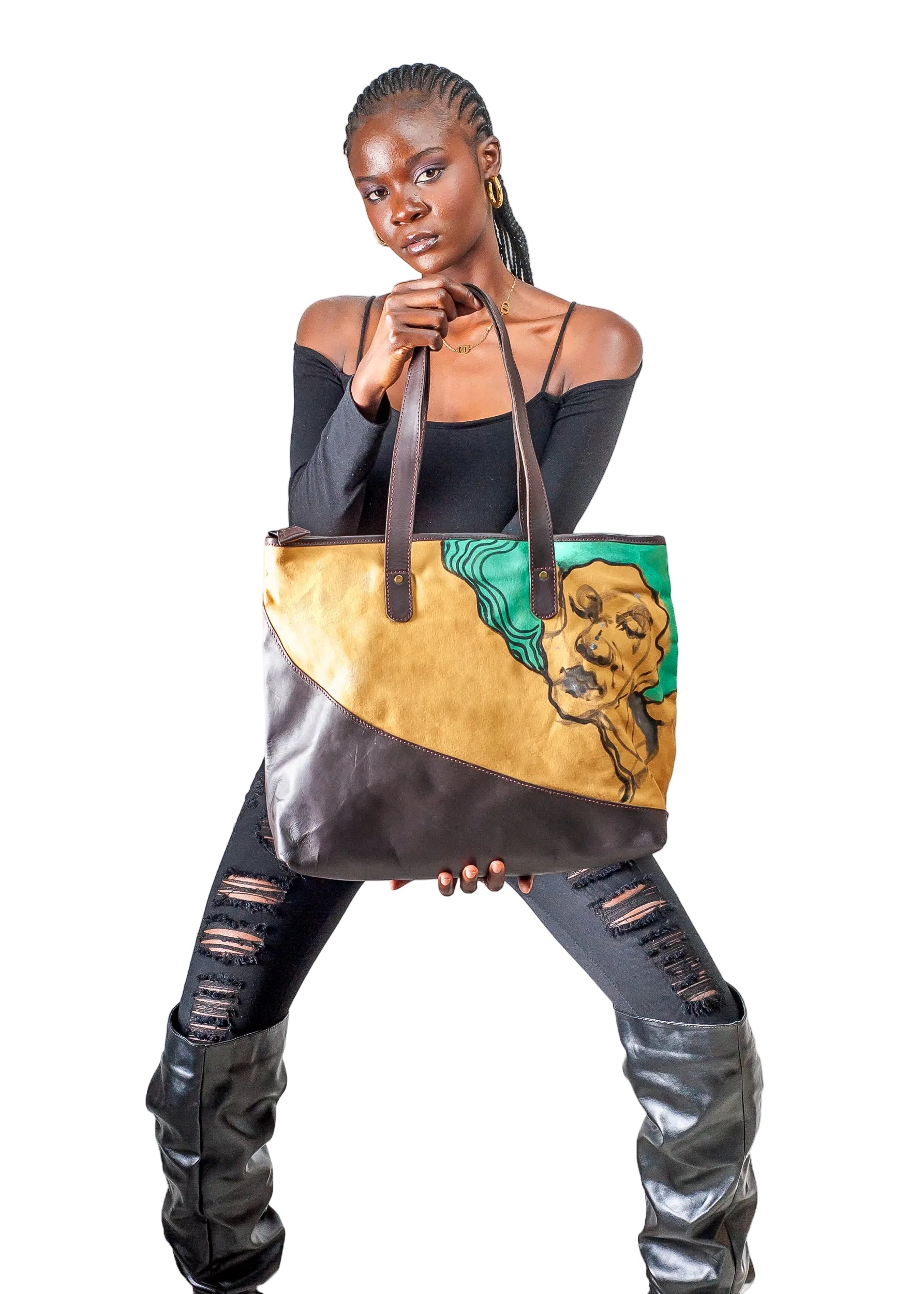 A woman modeling a large tote bag with a split tan and dark brown leather design, featuring a green and gold graphic illustration on the side, set against a plain white background.