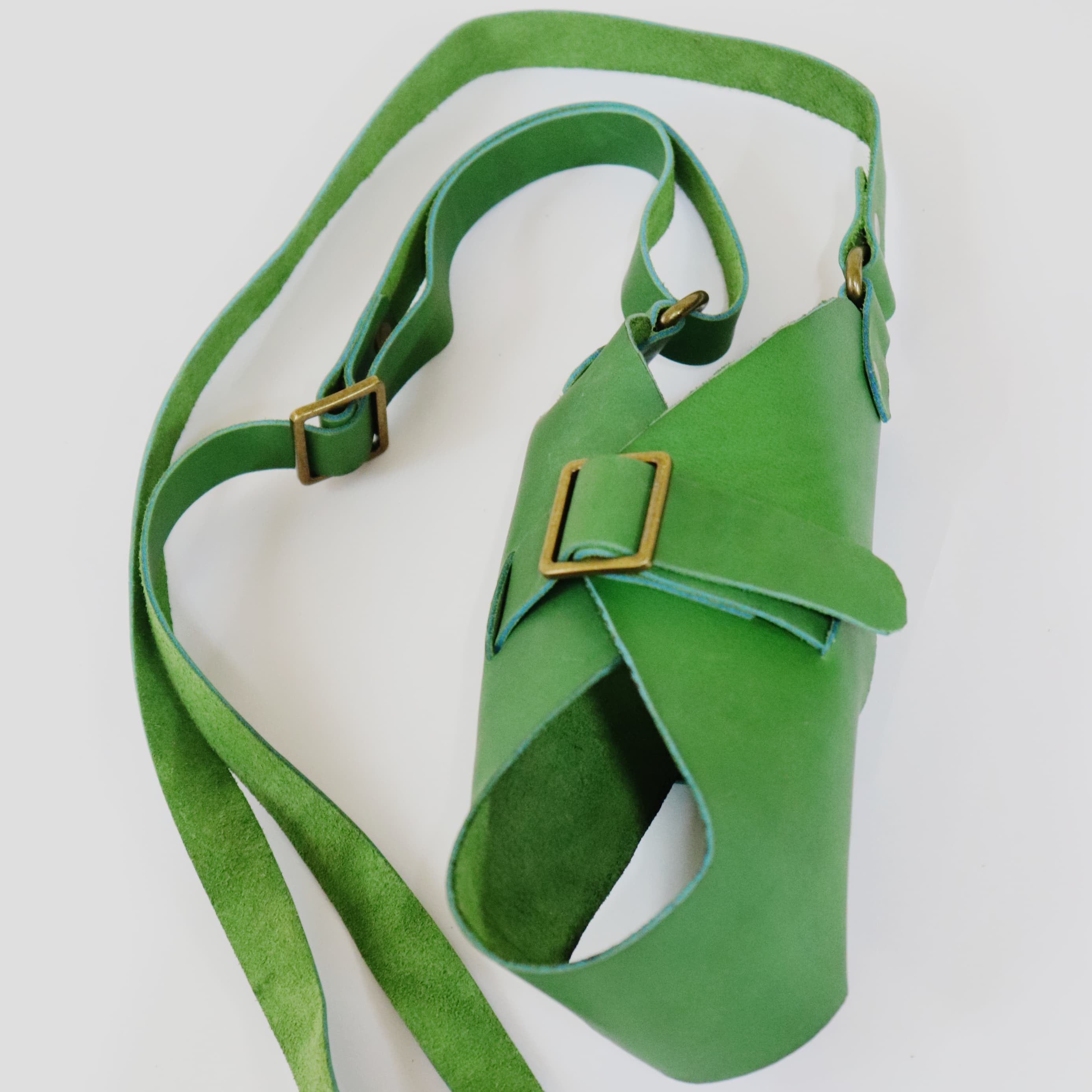 A bright green leather crossbody bag with a wide adjustable strap and gold-tone buckle details, photographed on a clean white background.