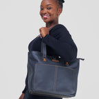 Woman holding a large blue tote bag against a plain background