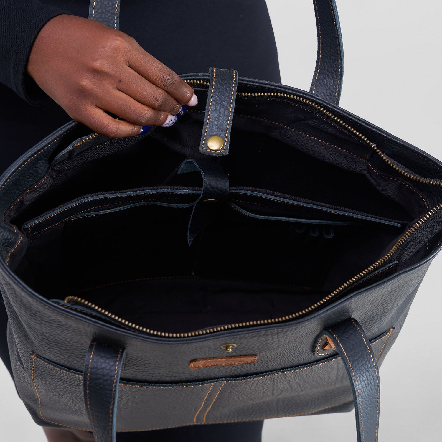 Person holding a dark blue handbag with visible interior and handles.