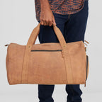Person holding a brown leather duffel bag against a plain background
