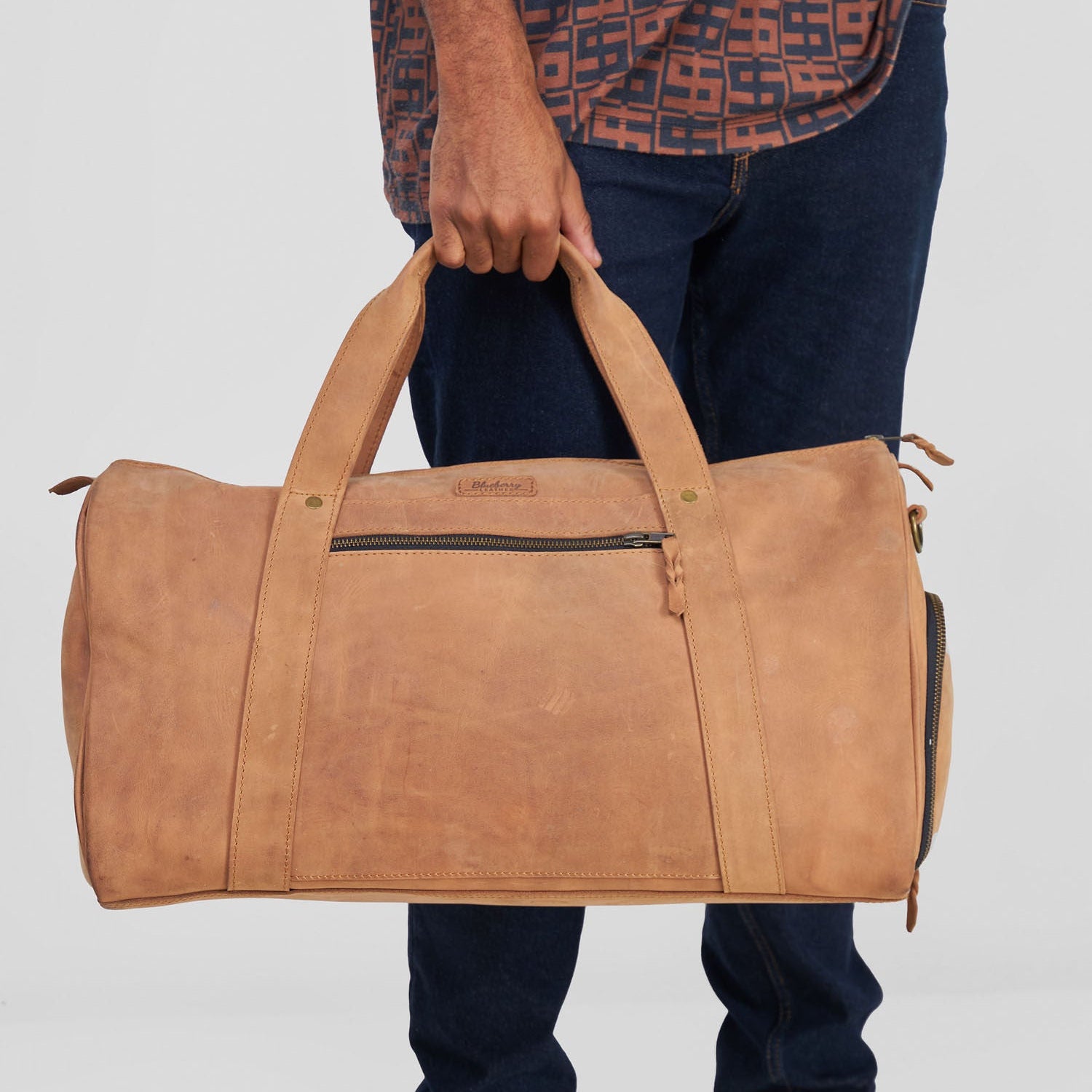 Person holding a brown leather duffel bag against a plain background