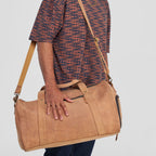 Man holding a brown leather duffel bag against a plain background