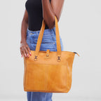 Person holding a tan leather tote bag against a plain background