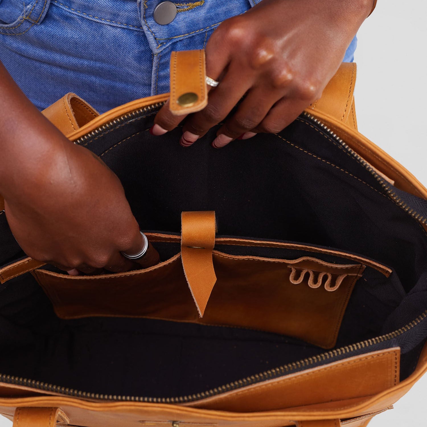 Person opening a brown leather bag with a white background