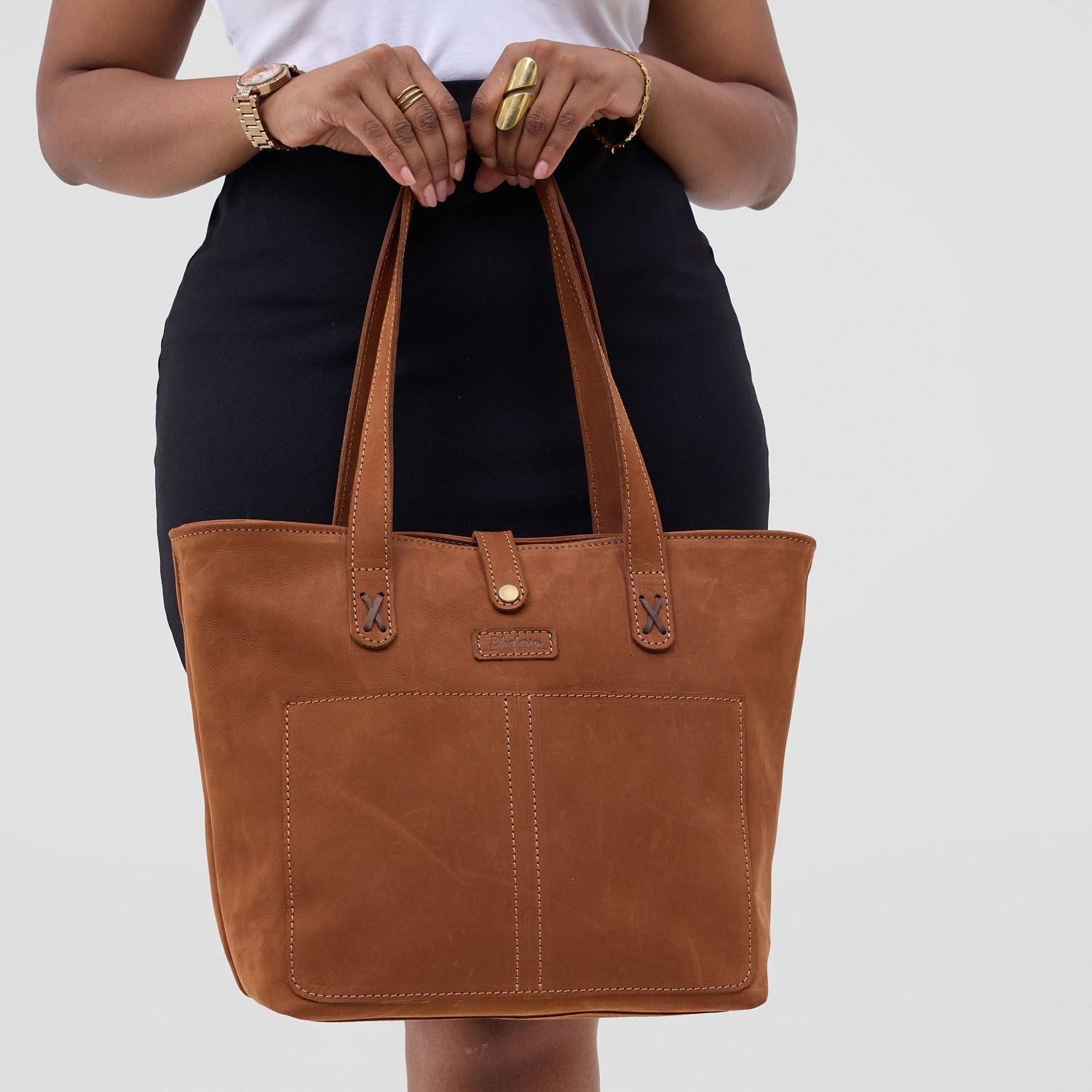Brown leather tote bag held by a person on a white background