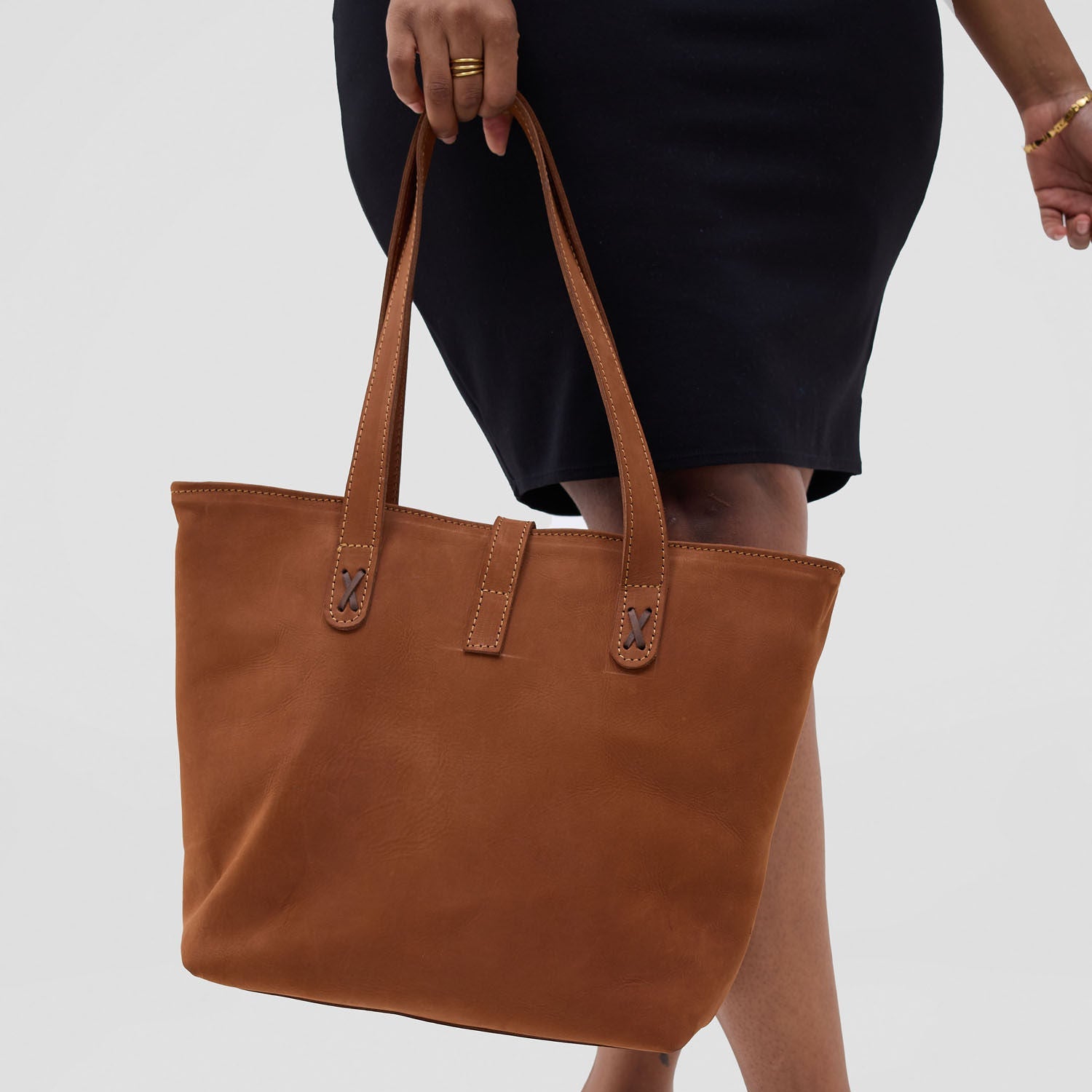 Brown tote bag held by a person wearing black shoes on a white background