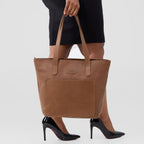Brown tote bag held by a person wearing black high heels on a white background