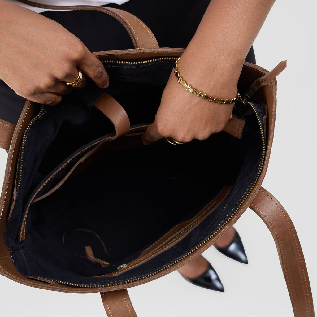 Person opening a brown leather bag with black interior on a light gray background