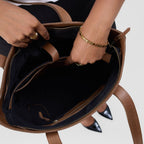Person opening a brown leather bag with black interior on a light gray background