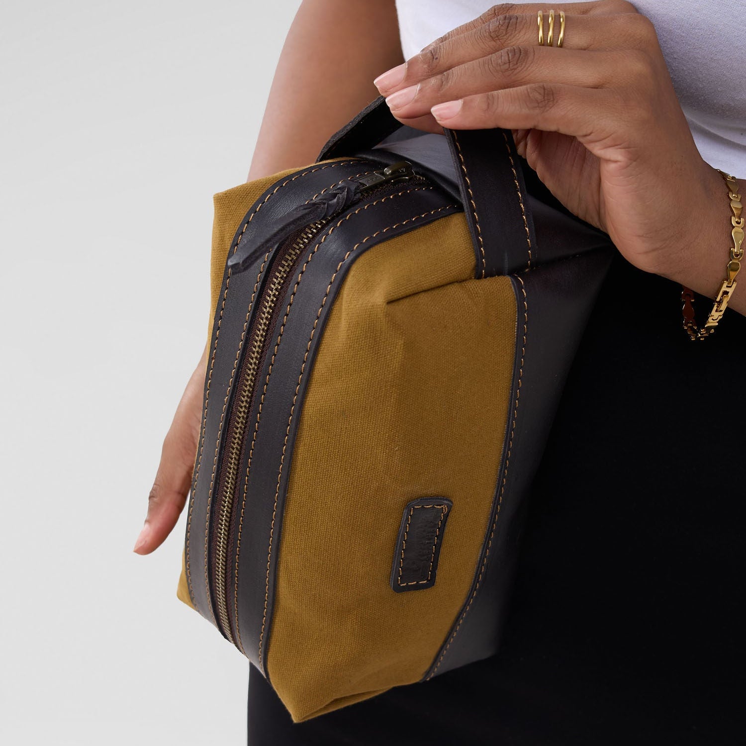Person holding a brown and black leather bag against a white background