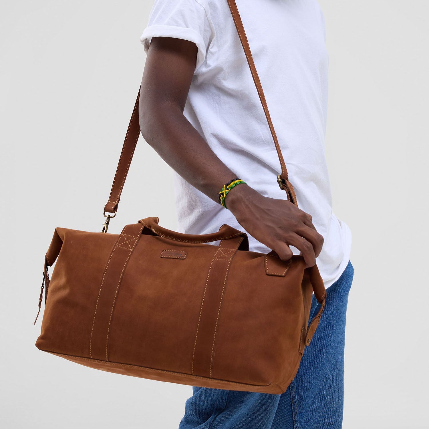 Person holding a brown leather duffel bag against a plain background