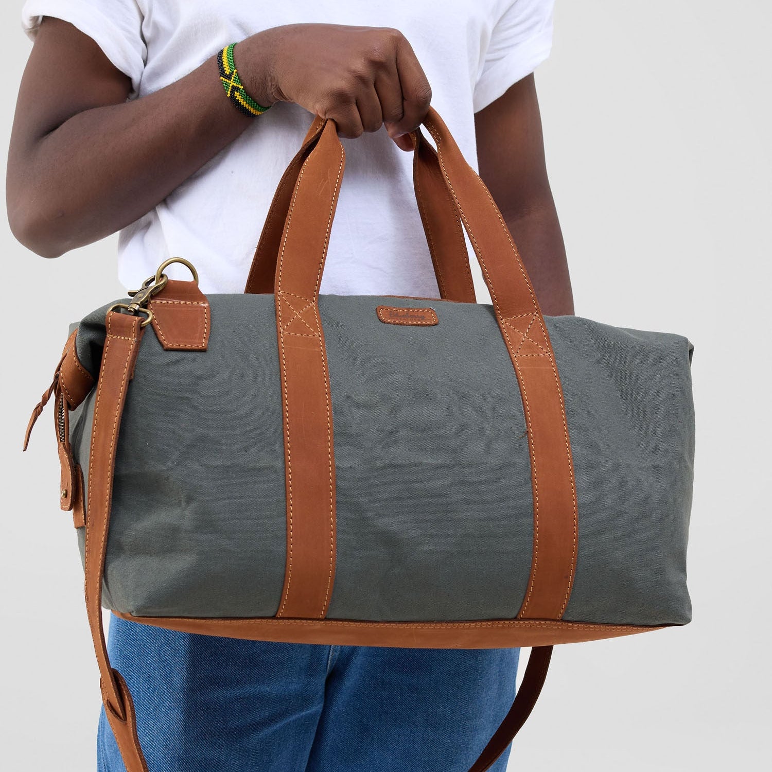 Person holding a gray duffel bag with brown handles and strap on a plain background