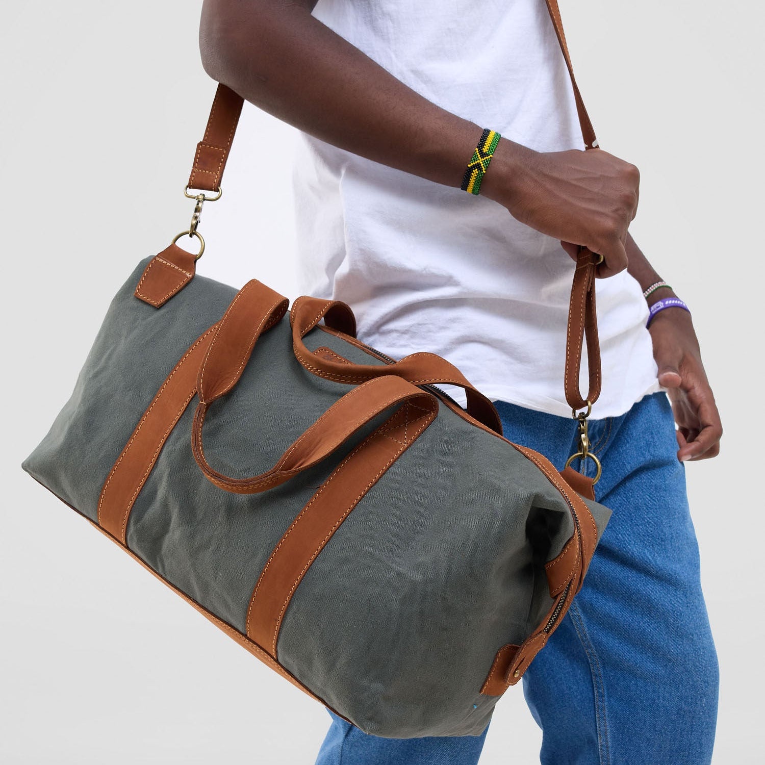 Person holding a gray duffel bag with brown leather straps on a plain background