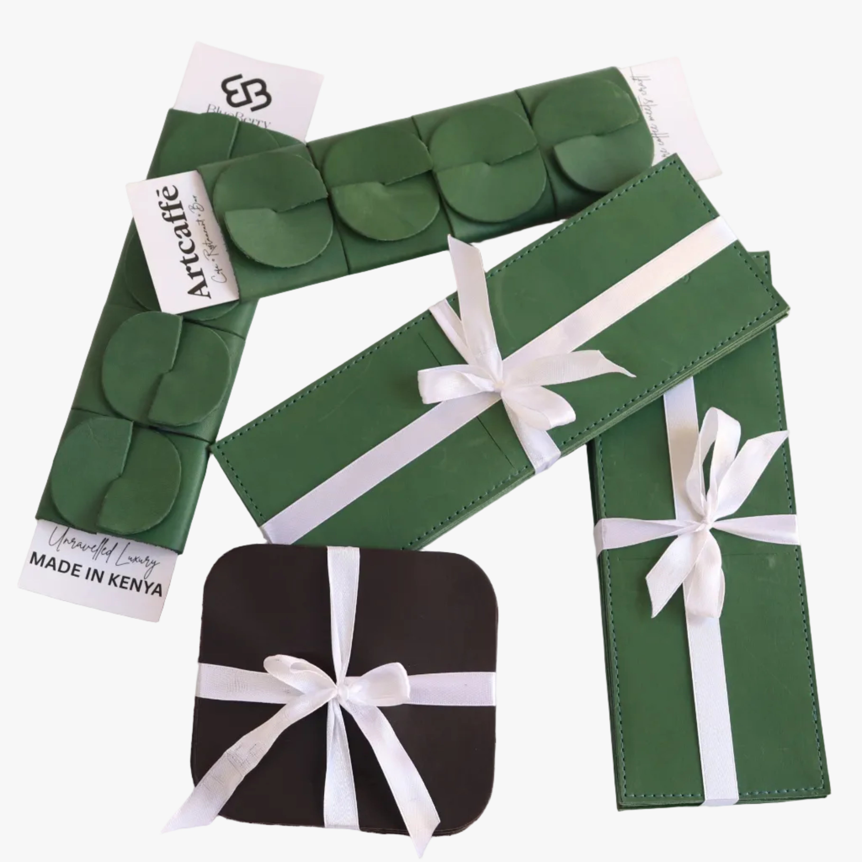 A set of green leather accessories, including a strap with a circular pattern, a long belt-like piece, and two rectangular pieces, arranged on a white background with two gift boxes wrapped in white ribbon. One box is green and one is black.