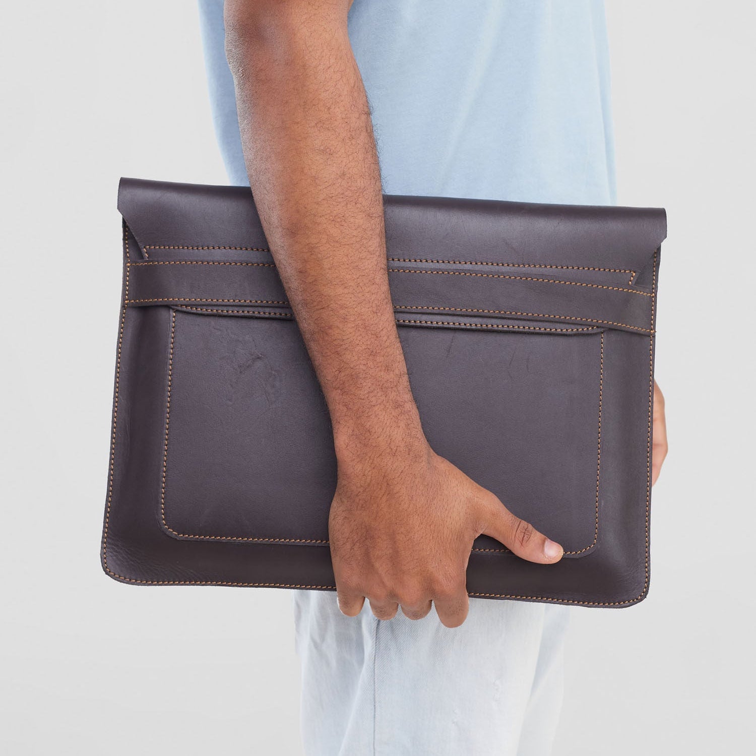 Person holding a dark brown leather clutch bag against a light background