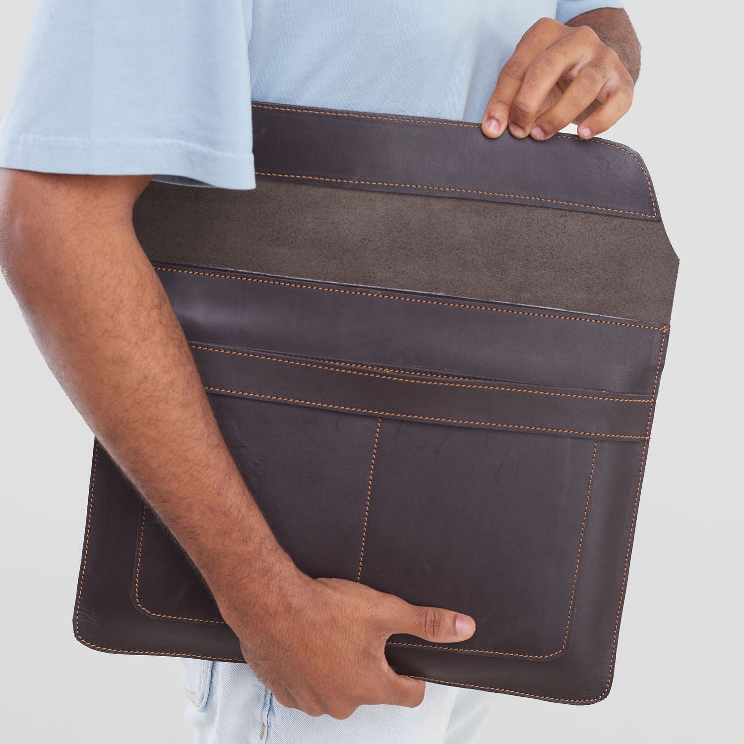 Person holding a brown leather briefcase against a plain background