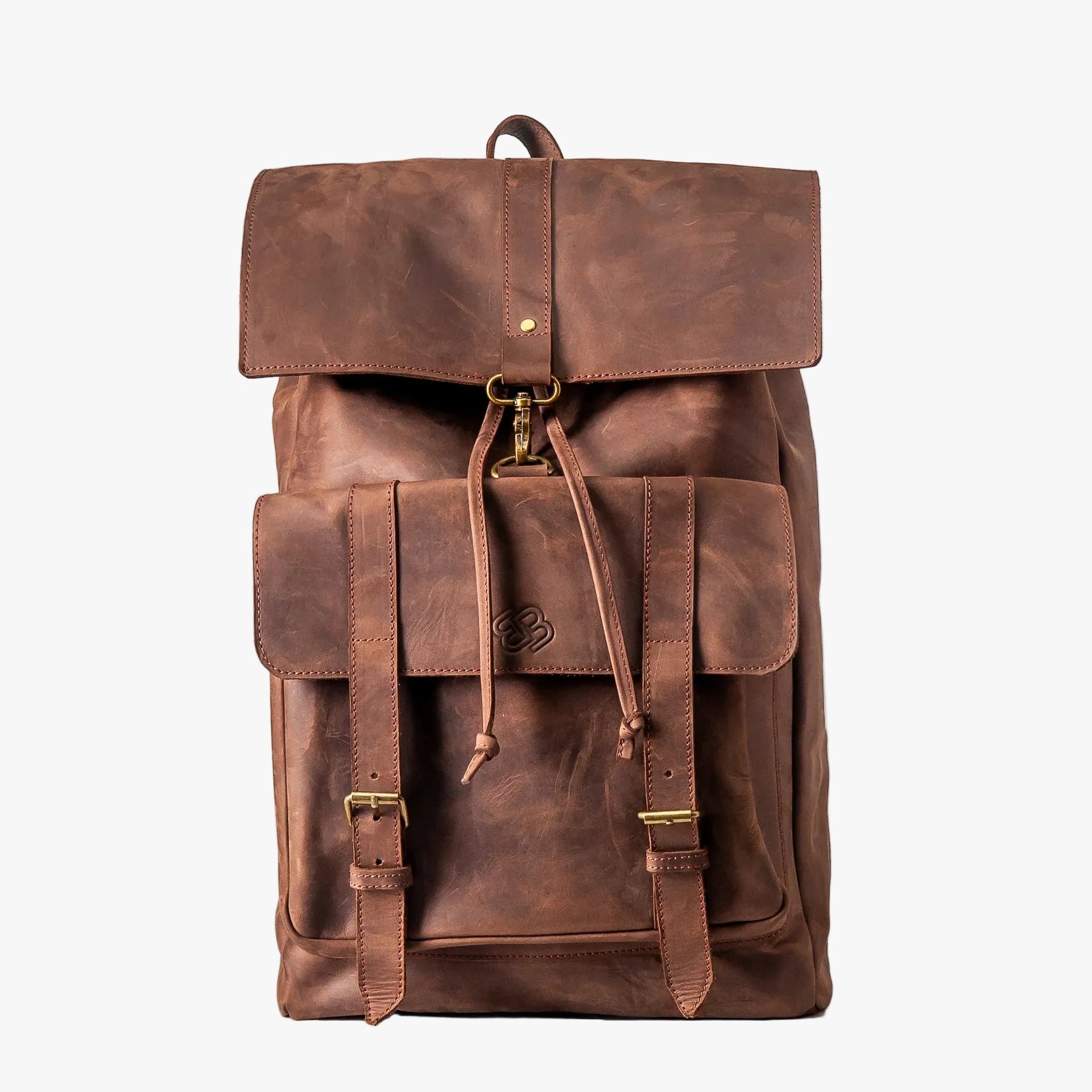 A brown leather backpack with a front flap pocket, drawstring closure, and brass-tone hardware, photographed against a plain white background.