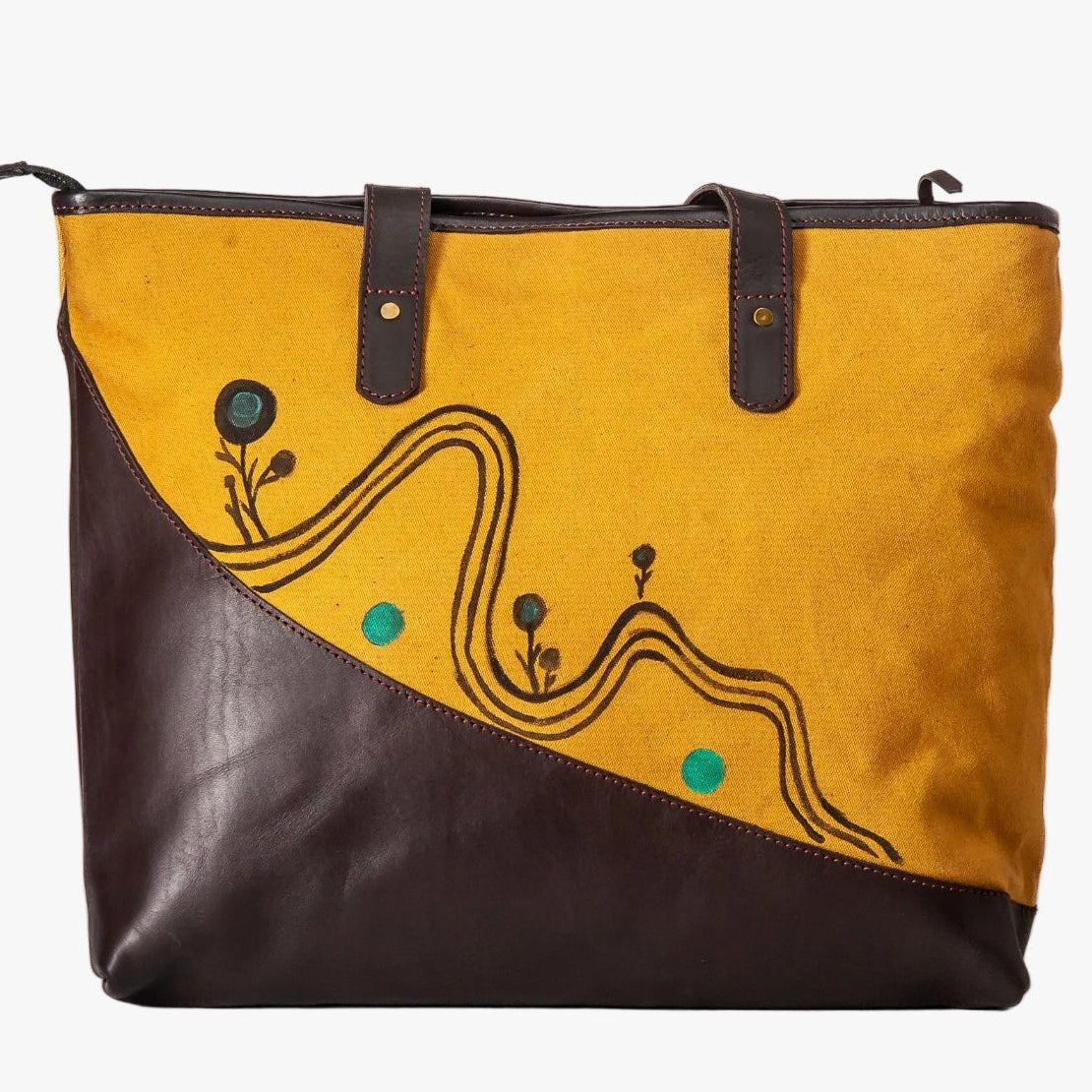 A tote bag with a diagonal split design, featuring a mustard yellow suede upper section with black abstract line art and small teal dots, and a dark brown leather lower section and handles.