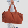 Person holding a brown duffel bag with a neutral background