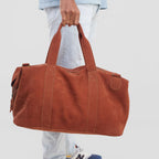 Person holding a brown duffel bag with a neutral background