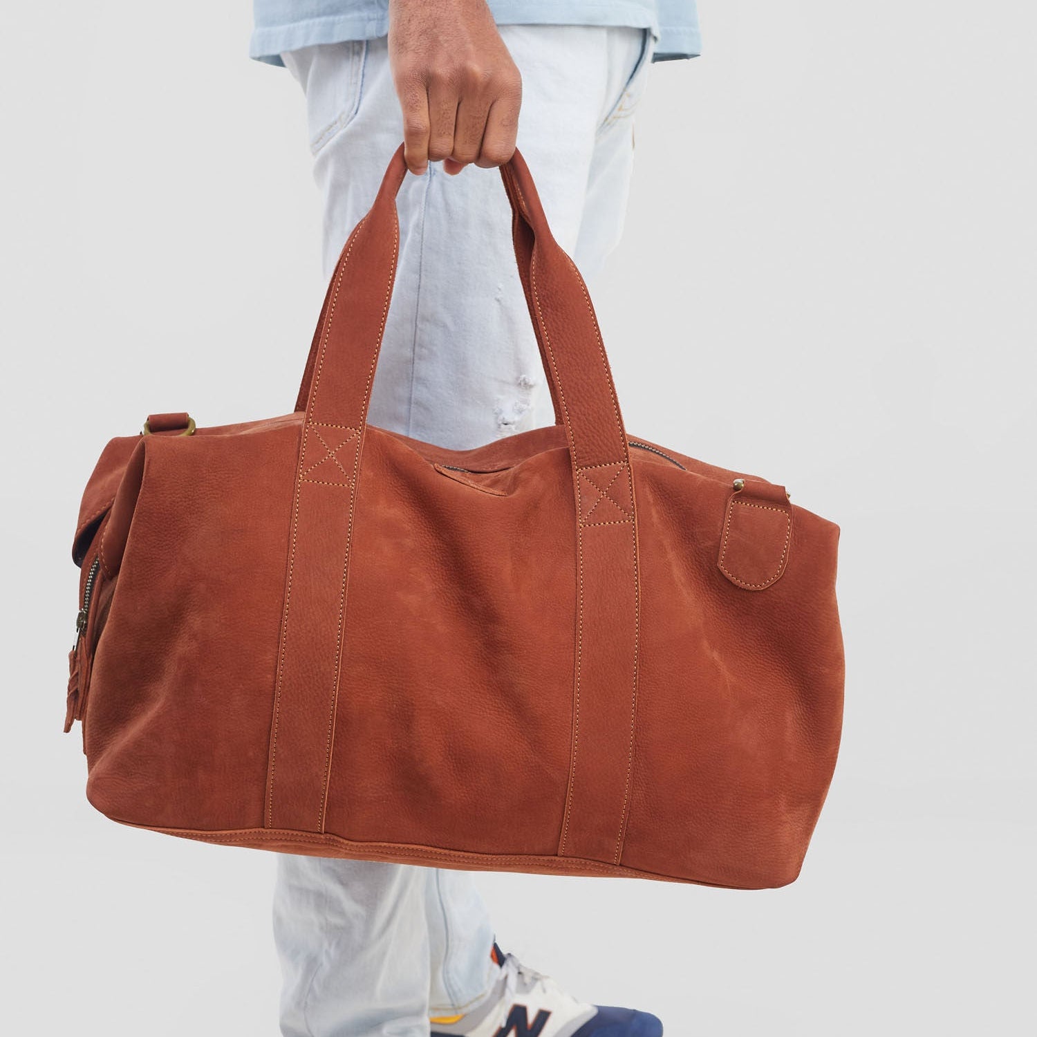 Person holding a brown duffel bag with a neutral background