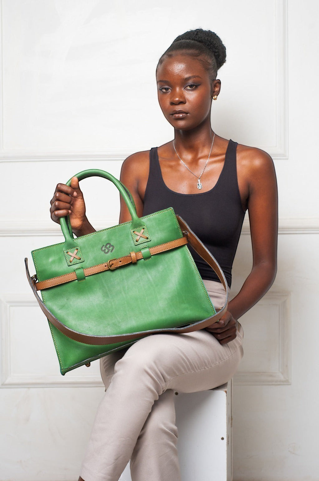 Model holding a forest green Blueberry Leather Duma cowhide tote bag with a tan adjustable buckle strap.