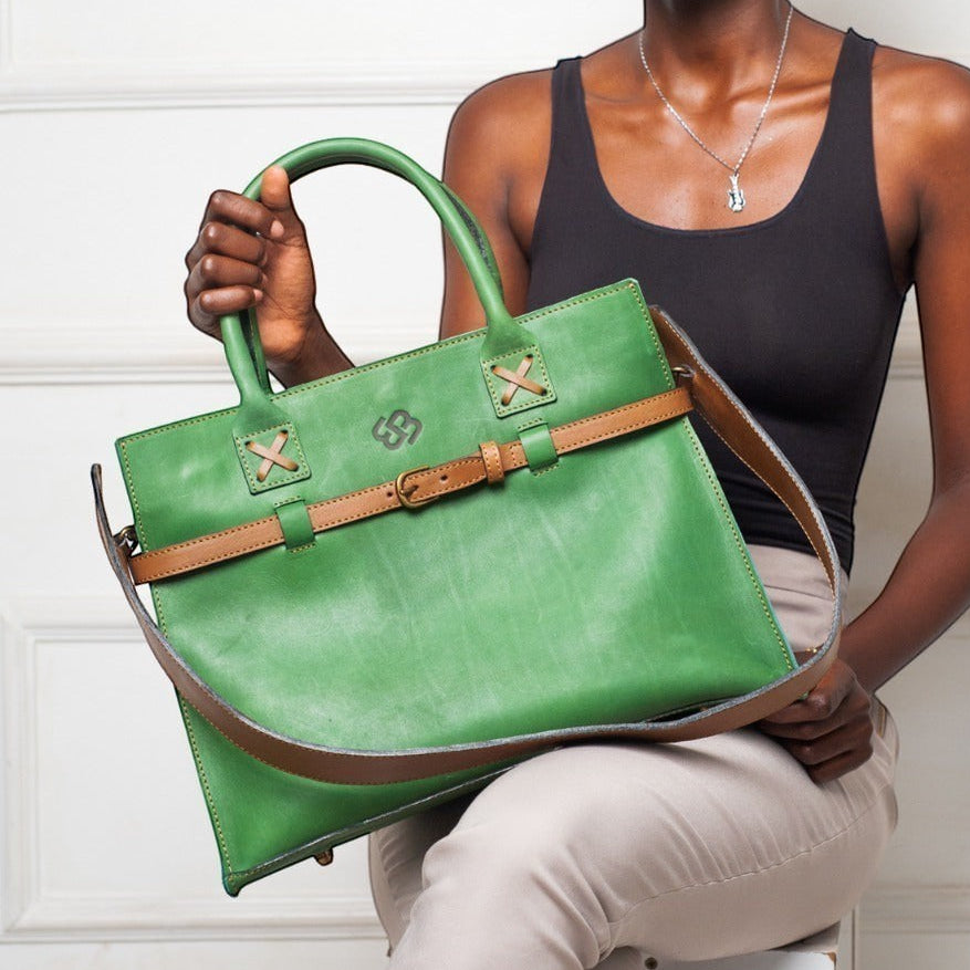 Model holding a forest green Blueberry Leather Duma cowhide tote bag with a tan adjustable buckle strap.