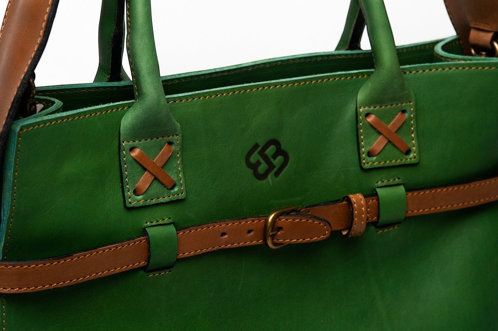 Blueberry Leather Duma tote in forest green cowhide leather with tan buckle strap and cross-stitched handle detail.