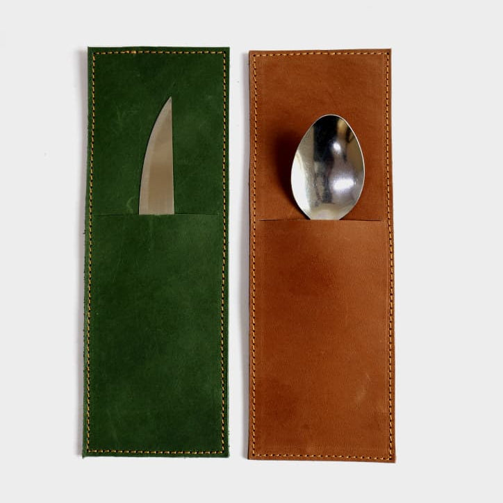 A set of two leather cutlery holders on a light gray background. The left holder is dark green suede with a knife blade visible in the pocket, and the right holder is brown leather with a spoon resting in the pocket.