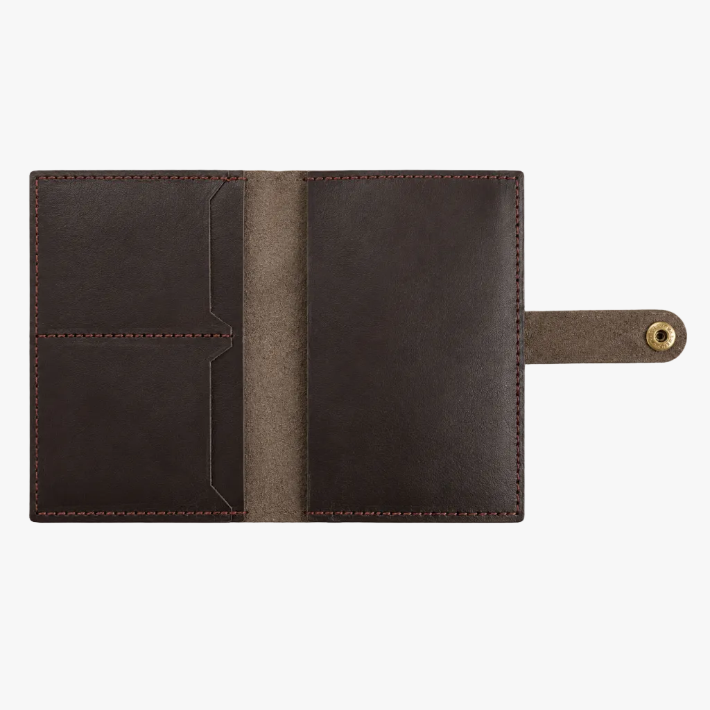 A dark brown leather passport cover or document holder shown open on a clean white background, featuring stitched edges, interior card slots, and a strap with a brass grommet.