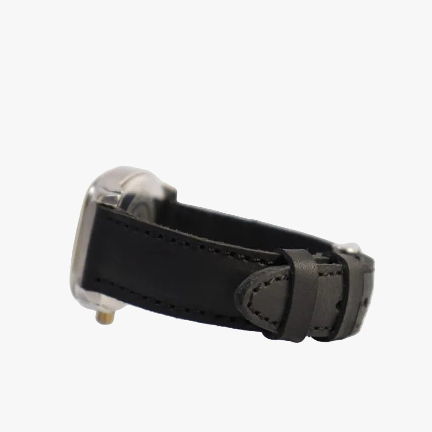 A close-up shot of a watch strap, showing a black leather band with a silver-toned metal buckle and case end, resting on a plain white surface.